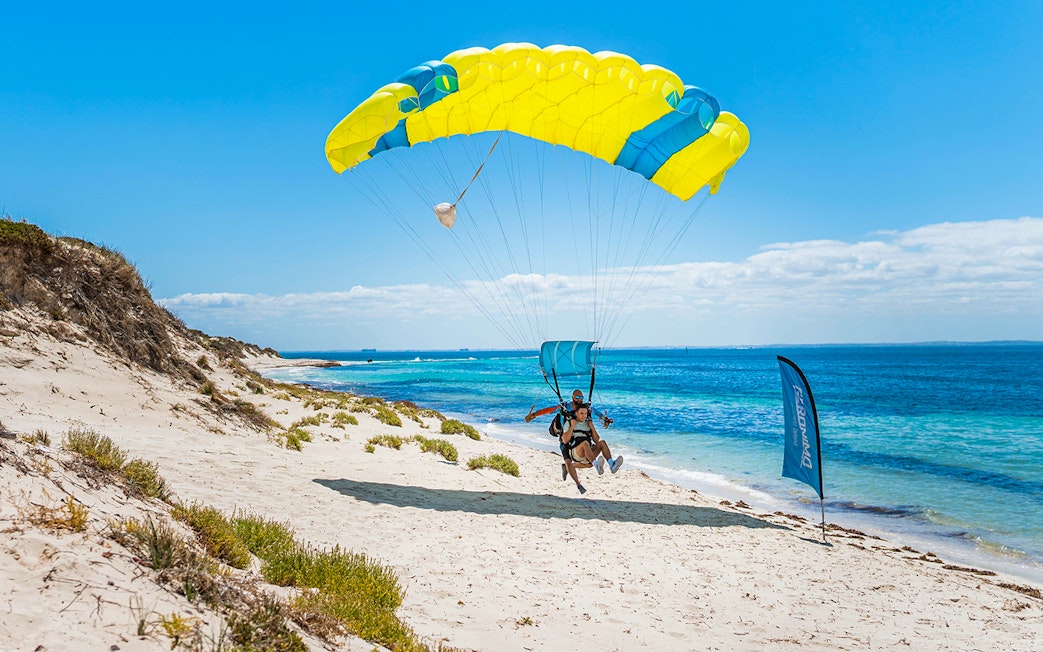 Instructor and guest landing with parachute on Rottnest Island beach.