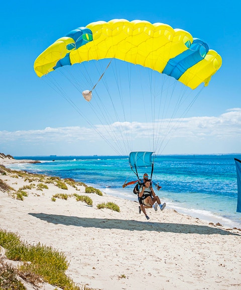Instructor and guest landing with parachute on Rottnest Island beach.