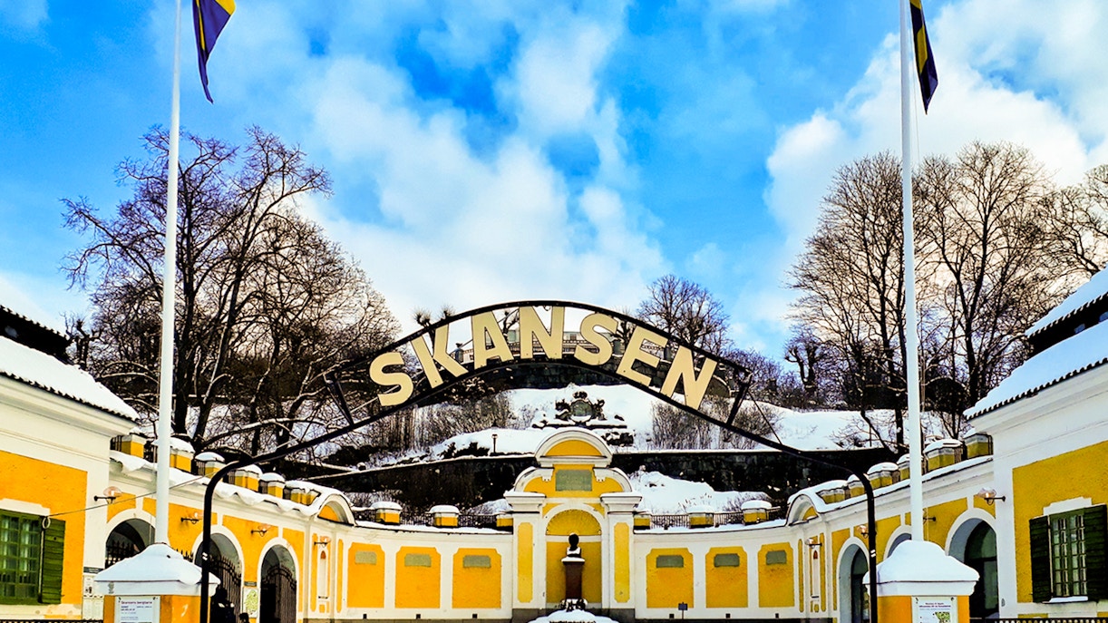 Skansen entrance with yellow buildings and snow-covered trees in Stockholm.