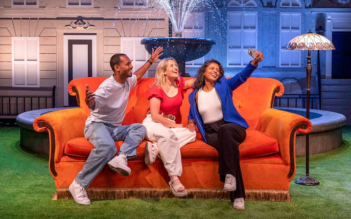 Visitors on an orange couch at The FRIENDS™ Experience, posing for a selfie near a fountain.