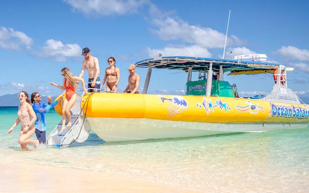 Tourists disembarking a boat onto a sandy beach during a Great Barrier Reef guided snorkel tour.