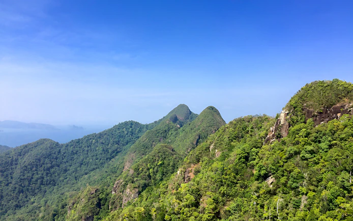 Langkawi lush green hills under clear blue sky, ideal for bird watching tour.