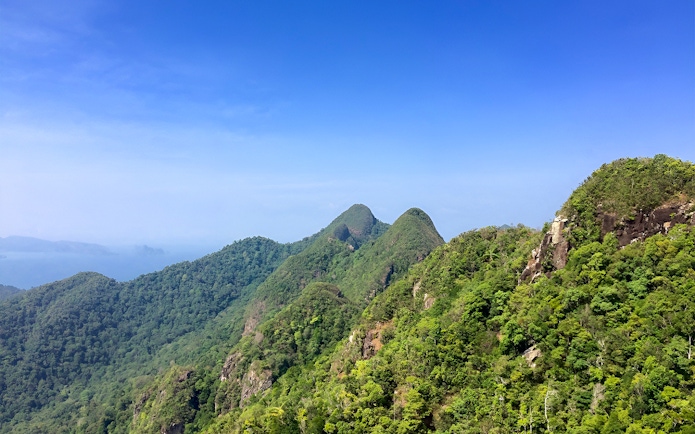 Langkawi lush green hills under clear blue sky, ideal for bird watching tour.