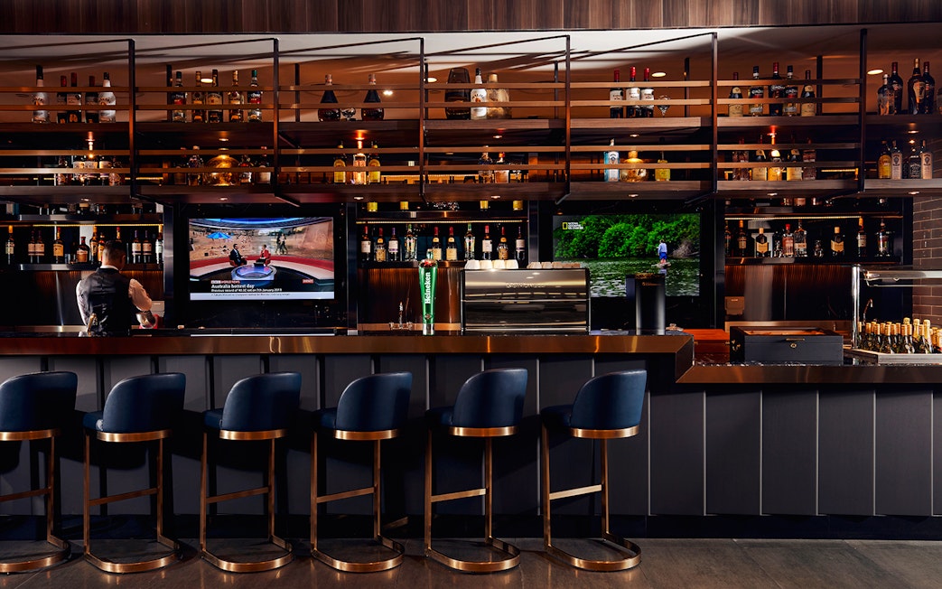 Bar area at Plaza Premium Lounge, Dubai International Airport, with seating and TV screens.