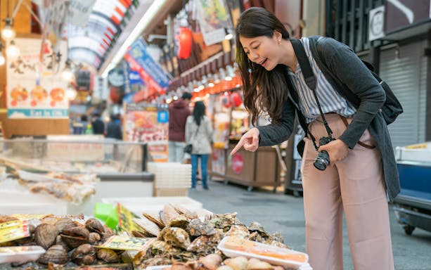 Woman exploring seafood stall at Osaka market during food tour.