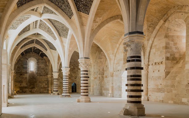 Interior of Maniace Castle with vaulted ceilings and striped columns during guided tour.