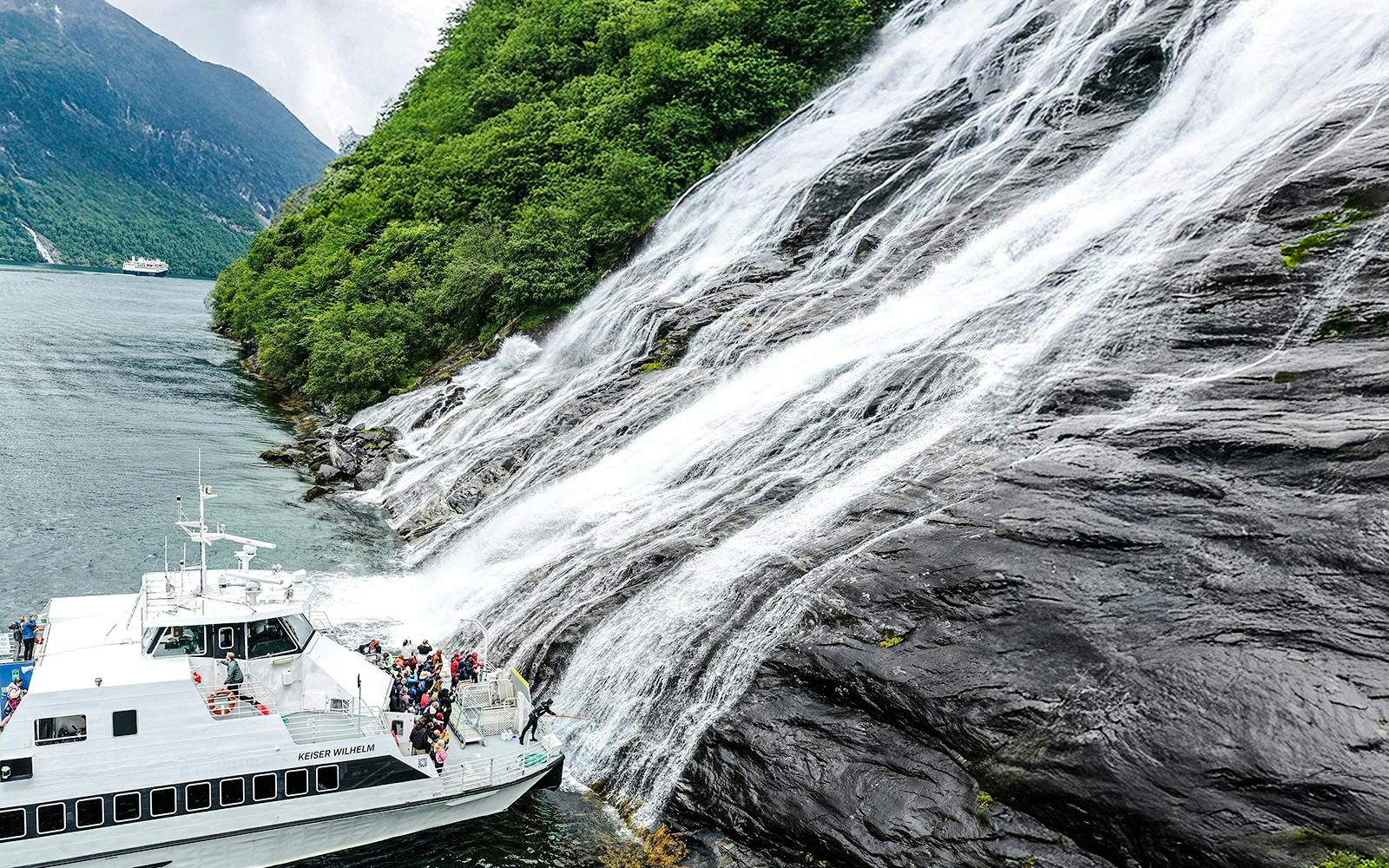 Boat near waterfall in Geiranger Fjord during a tour with visitors tasting the waterfall.