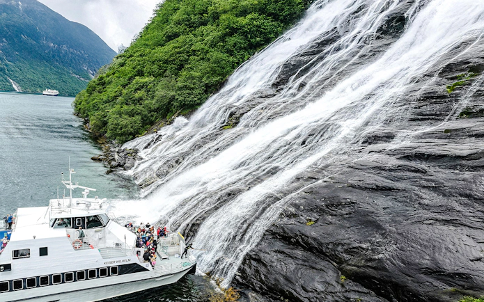 Boat near waterfall in Geiranger Fjord during a tour with visitors tasting the waterfall.