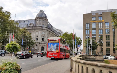 Red double-decker bus on a city tour in Düsseldorf, passing historic buildings.