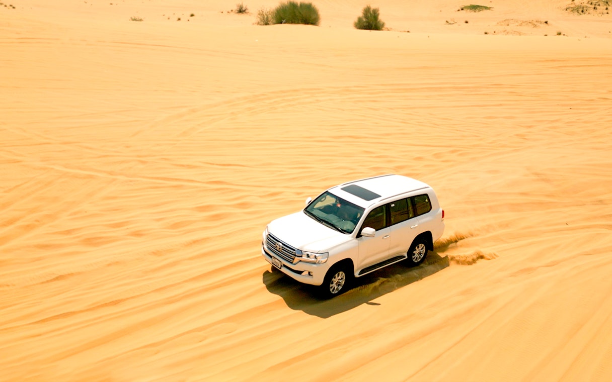 SUV driving through desert dunes during morning safari.