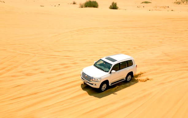 SUV driving through desert dunes during morning safari.
