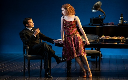 Man and woman in 1920s attire in a Leopoldstadt theater scene with gramophone and dining table.