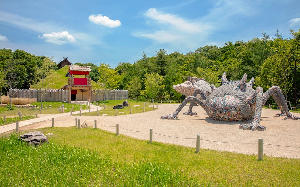 Giant creature sculpture at Ghibli Park's Mononoke Village, surrounded by greenery and traditional architecture.