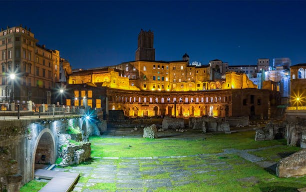 Roman Forum illuminated at night with ancient ruins and surrounding buildings.