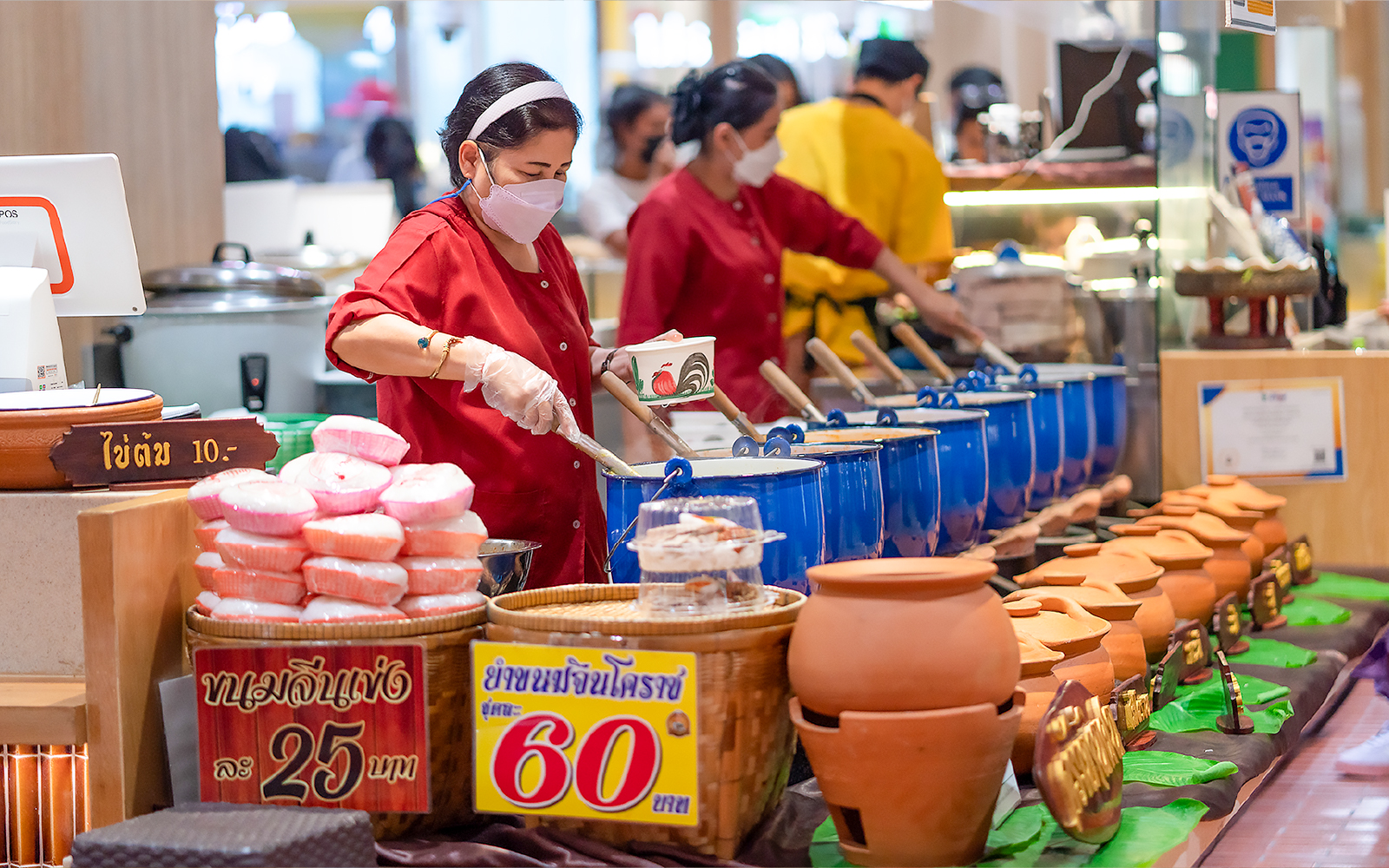 Woman serving Thai food from blue pots at Ayutthaya market stall.