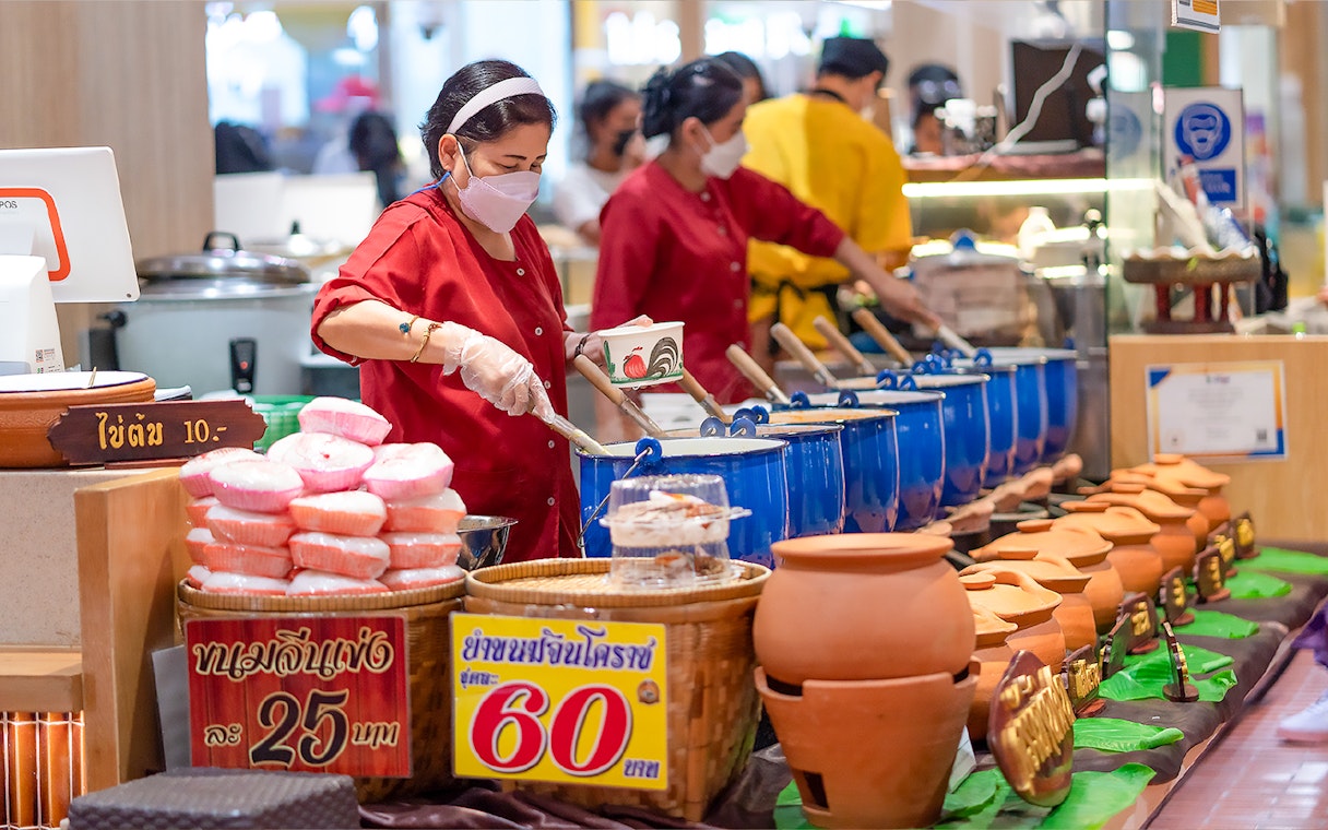 Woman serving Thai food from blue pots at Ayutthaya market stall.
