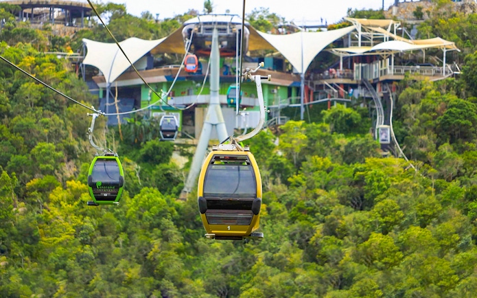 Langkawi SkyCab cable cars ascending over lush green hills toward the station.