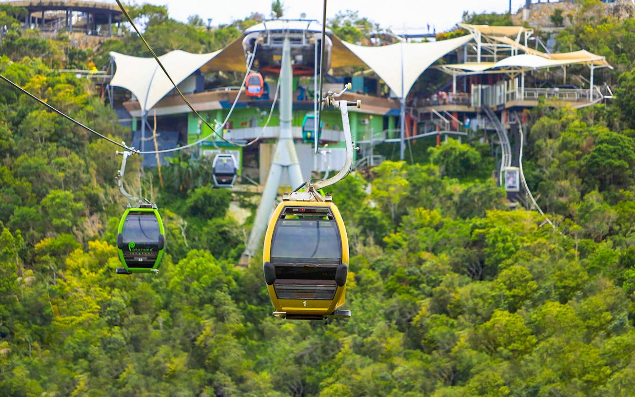 Langkawi SkyCab cable cars ascending over lush green hills toward the station.
