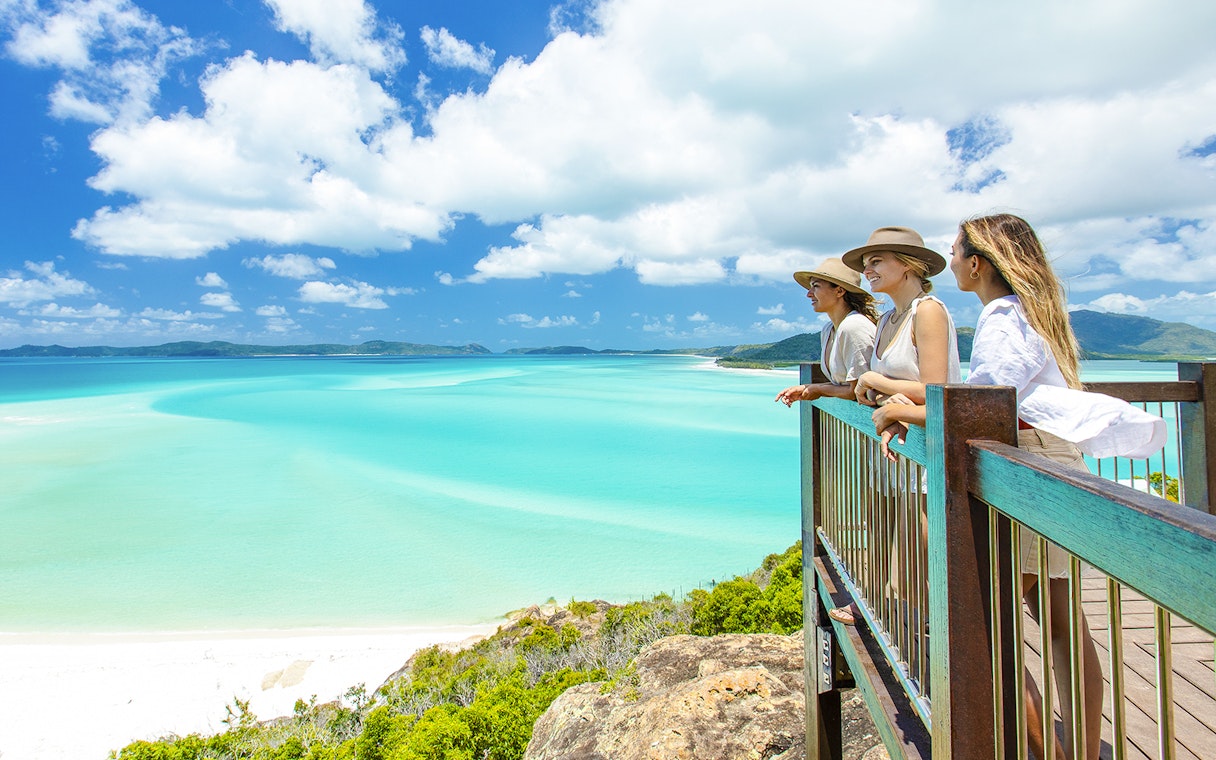 Tourists enjoying the view from Hill Inlet Lookout, Whitsundays, overlooking turquoise waters.