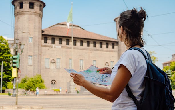 Tourist with map near historic building on Turin hop-on hop-off bus tour.