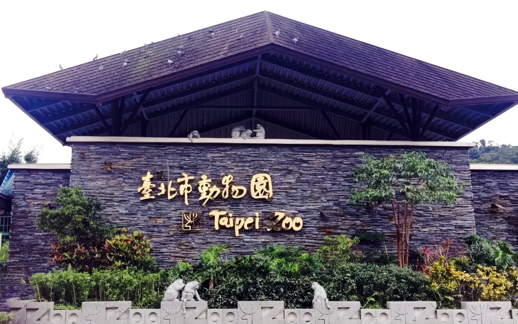 Taipei Zoo entrance sign with stone wall and greenery.