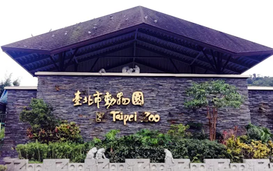 Taipei Zoo entrance sign with stone wall and greenery.