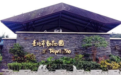 Taipei Zoo entrance sign with stone wall and greenery.