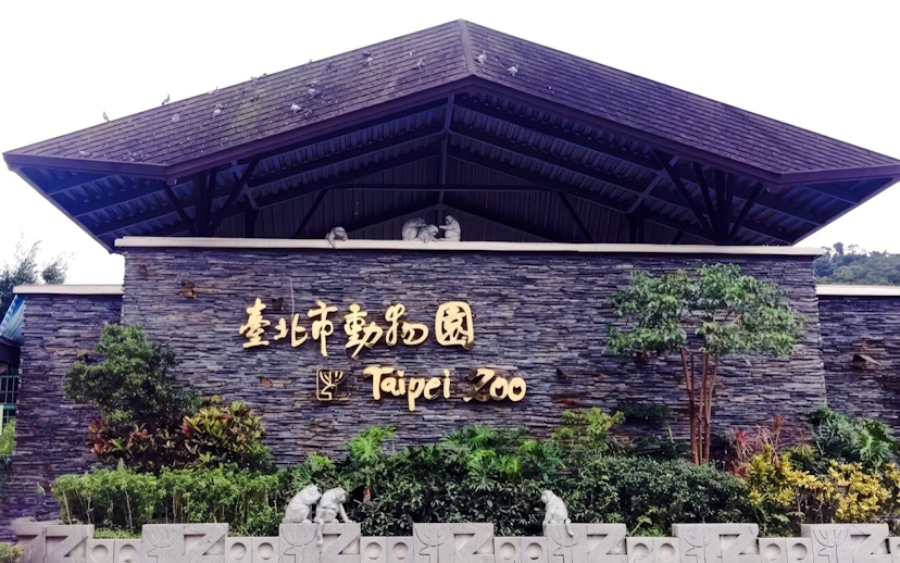 Taipei Zoo entrance sign with stone wall and greenery.