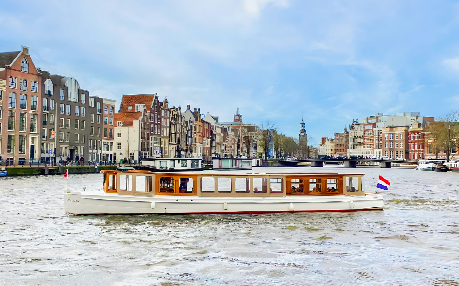 Saloon boat cruising on Amsterdam canal with historic buildings in the background.