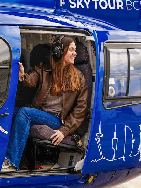 Tourist sitting in a blue helicopter with headset, ready for a sky tour.