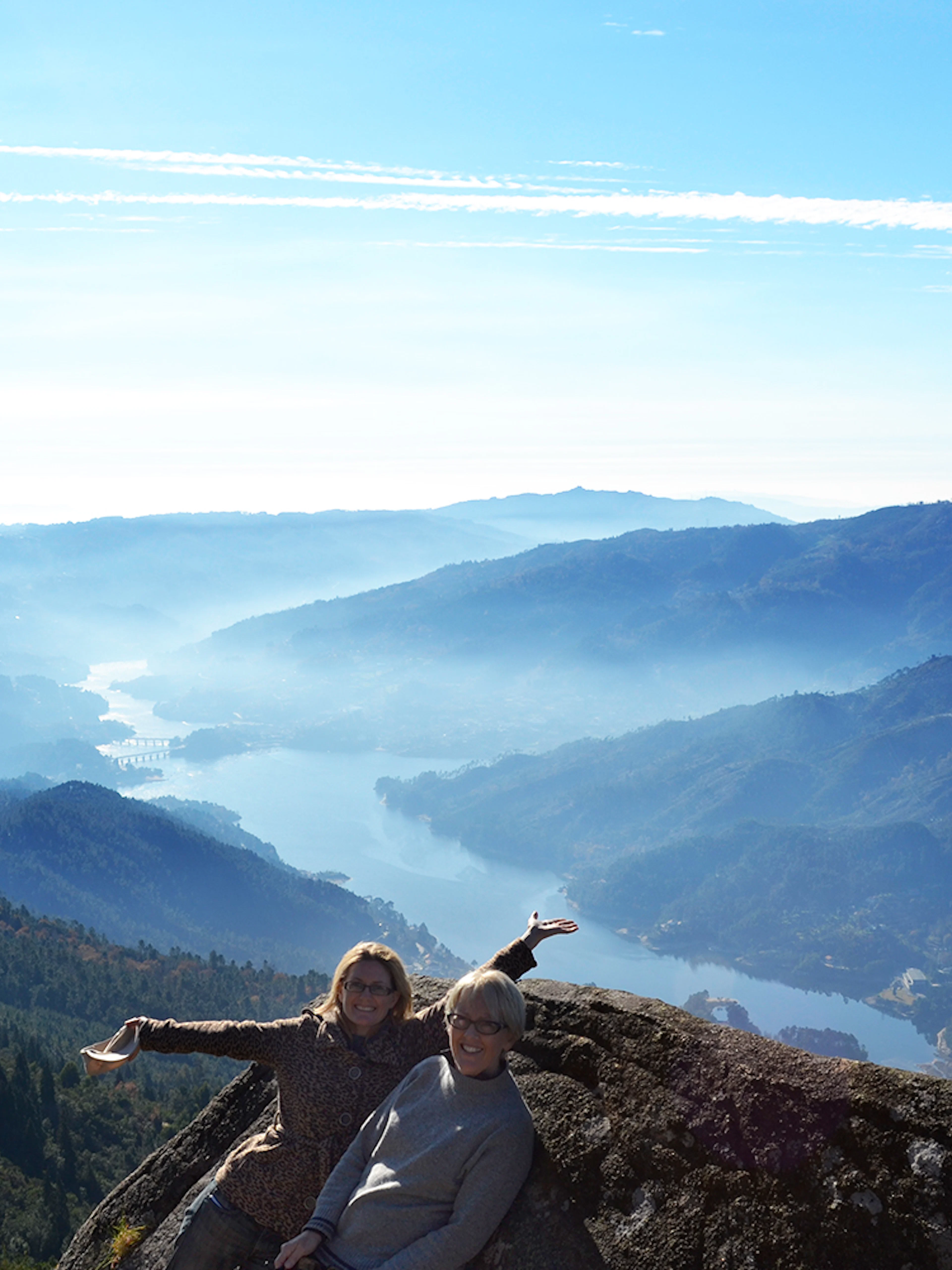 Two people enjoying a scenic view of Peneda Gerês National Park with mountains and a river below.