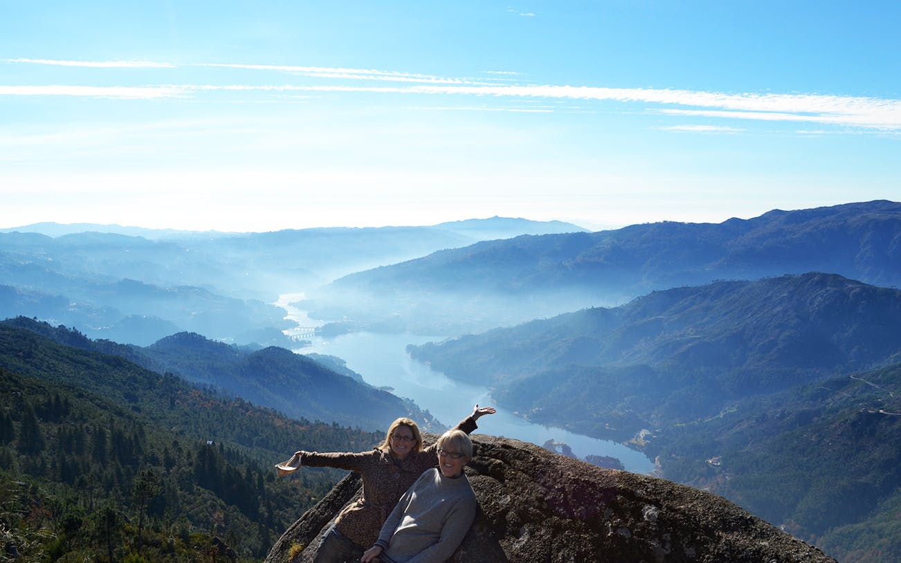 Two people enjoying a scenic view of Peneda Gerês National Park with mountains and a river below.