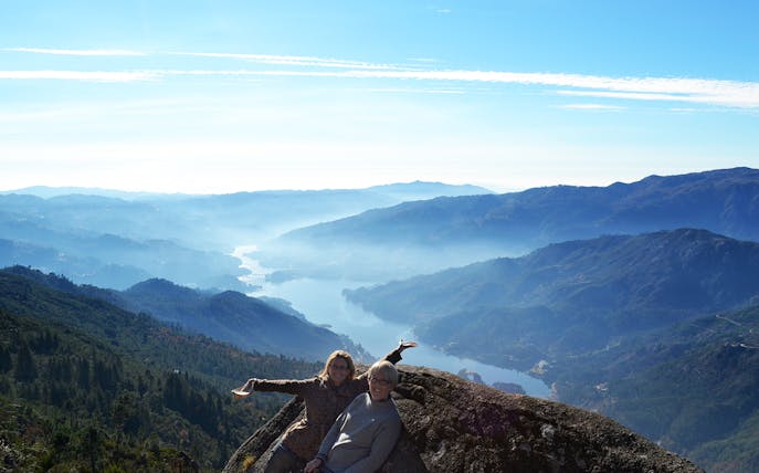 Two people enjoying a scenic view of Peneda Gerês National Park with mountains and a river below.