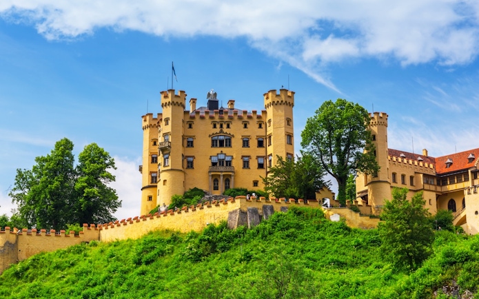 Hohenschwangau Castle surrounded by lush greenery under a blue sky.