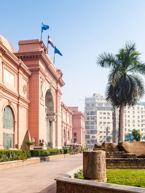 Exterior of the Egyptian Museum in Cairo with palm trees and ancient artifacts.