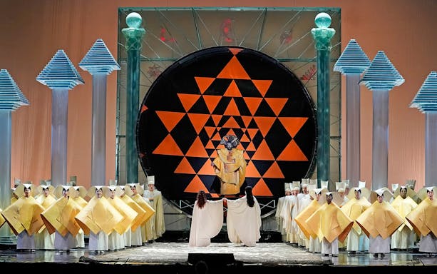 Opera performance of The Magic Flute with singers in geometric costumes on stage.