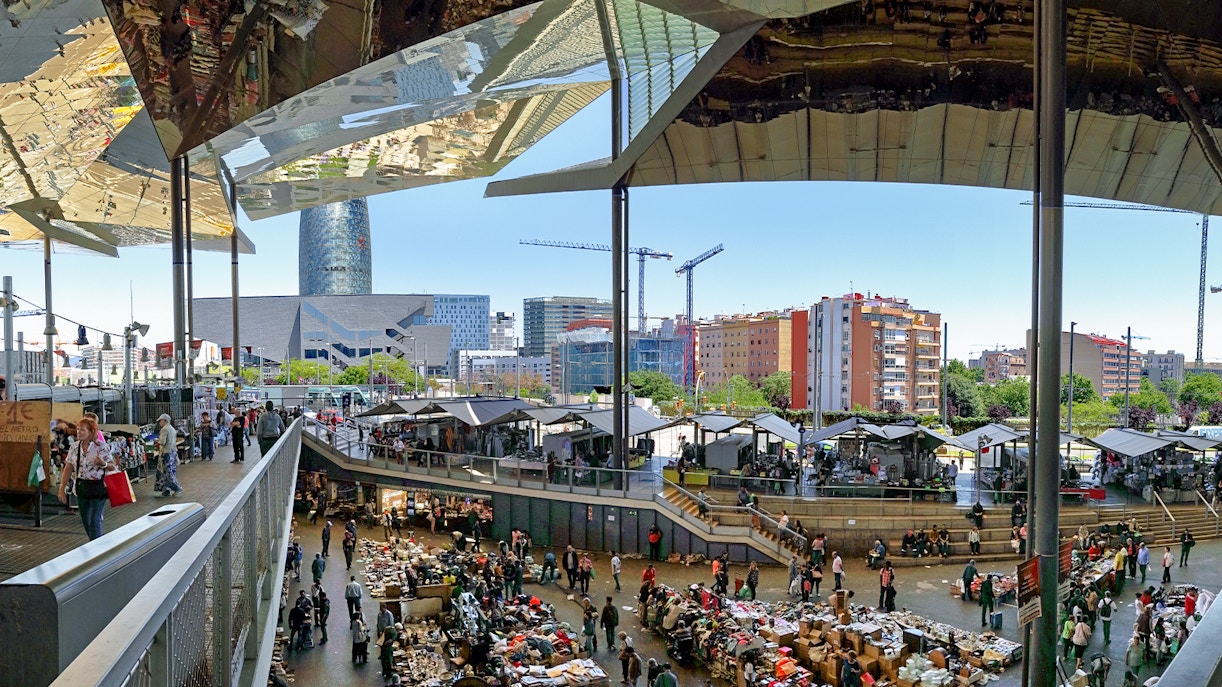 Encants Vells Flea Market in Barcelona with stalls and shoppers under a mirrored roof.
