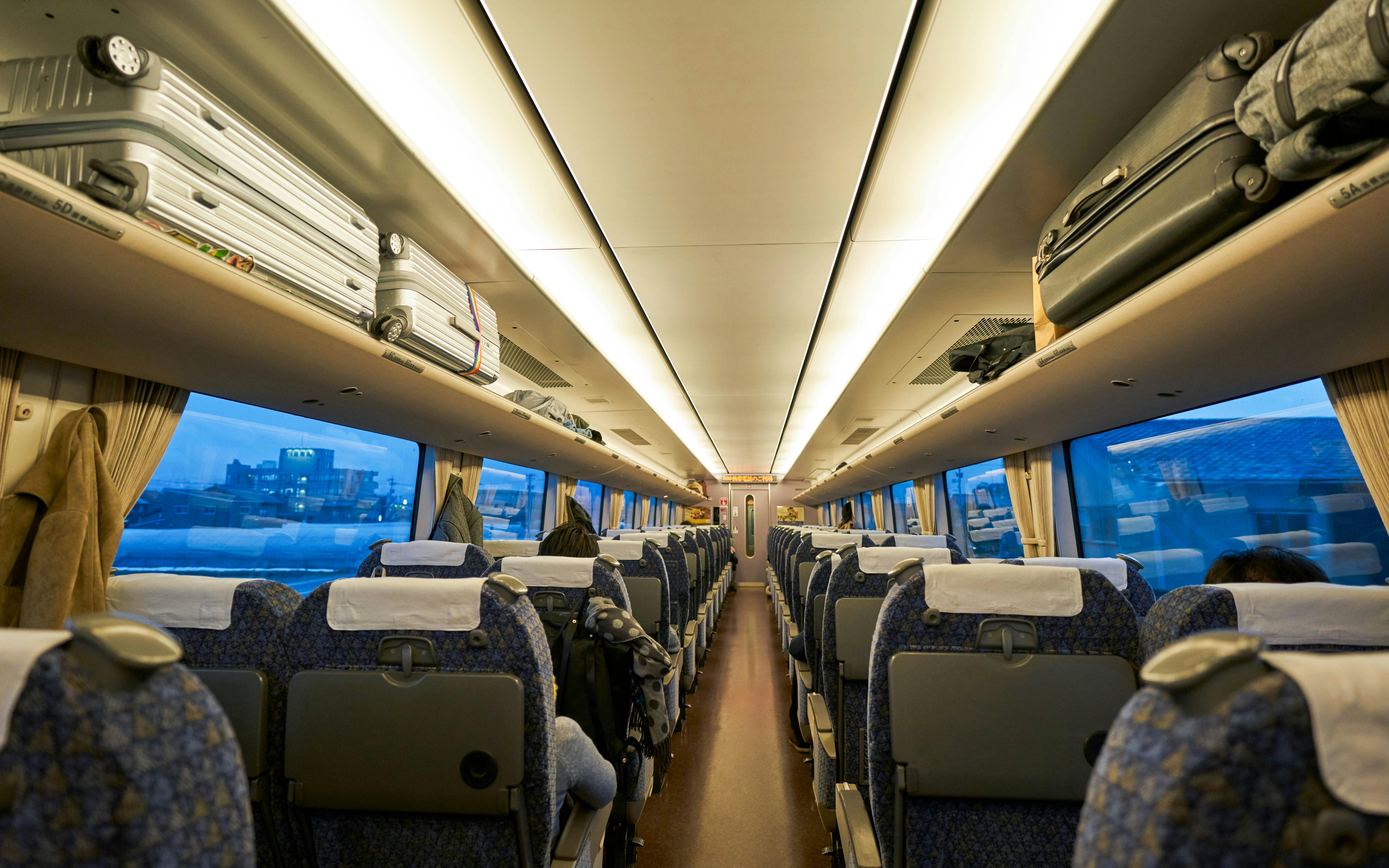 JR West Thunderbird train interior with central aisle and overhead luggage racks.