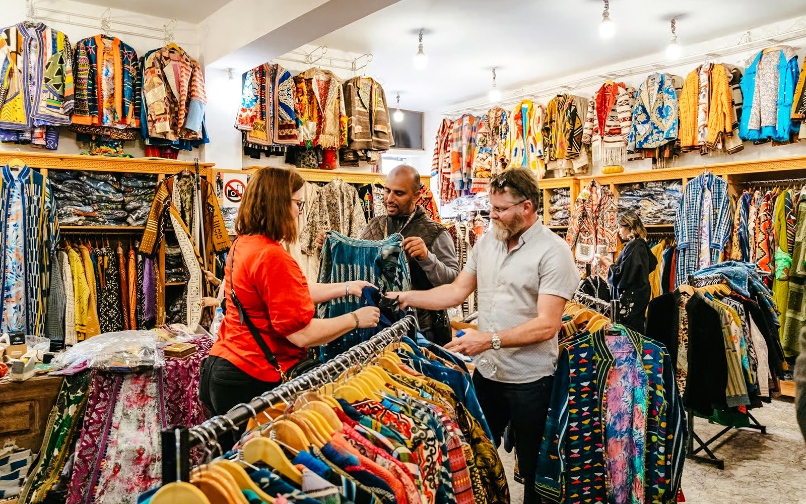 Shoppers exploring colorful garments in a Marrakech souk during a private shopping tour.