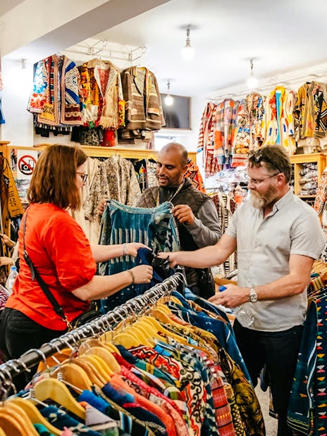 Shoppers exploring colorful garments in a Marrakech souk during a private shopping tour.