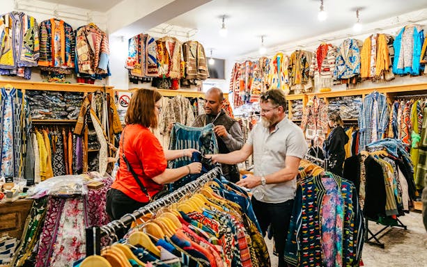 Shoppers exploring colorful garments in a Marrakech souk during a private shopping tour.