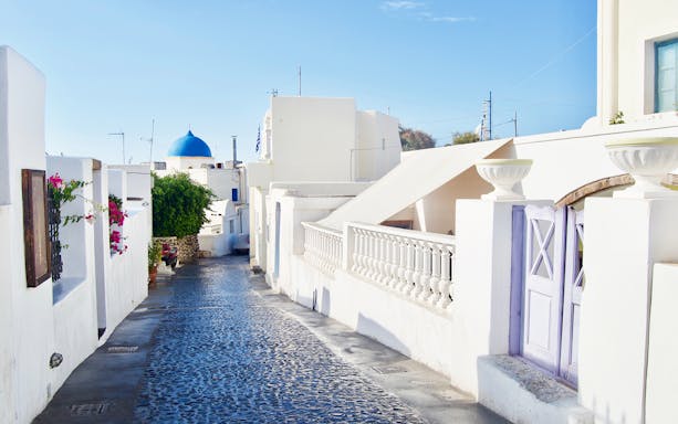 Cobbled street with white buildings and blue dome in Santorini, Greece.