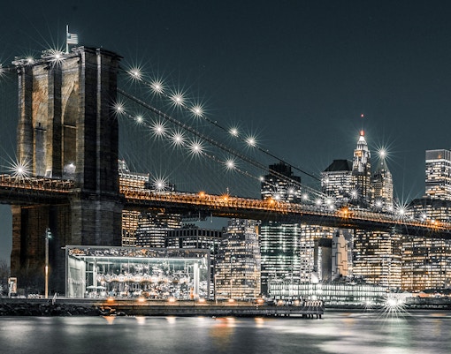 Brooklyn Bridge and NYC skyline illuminated at night during harbor lights cruise.