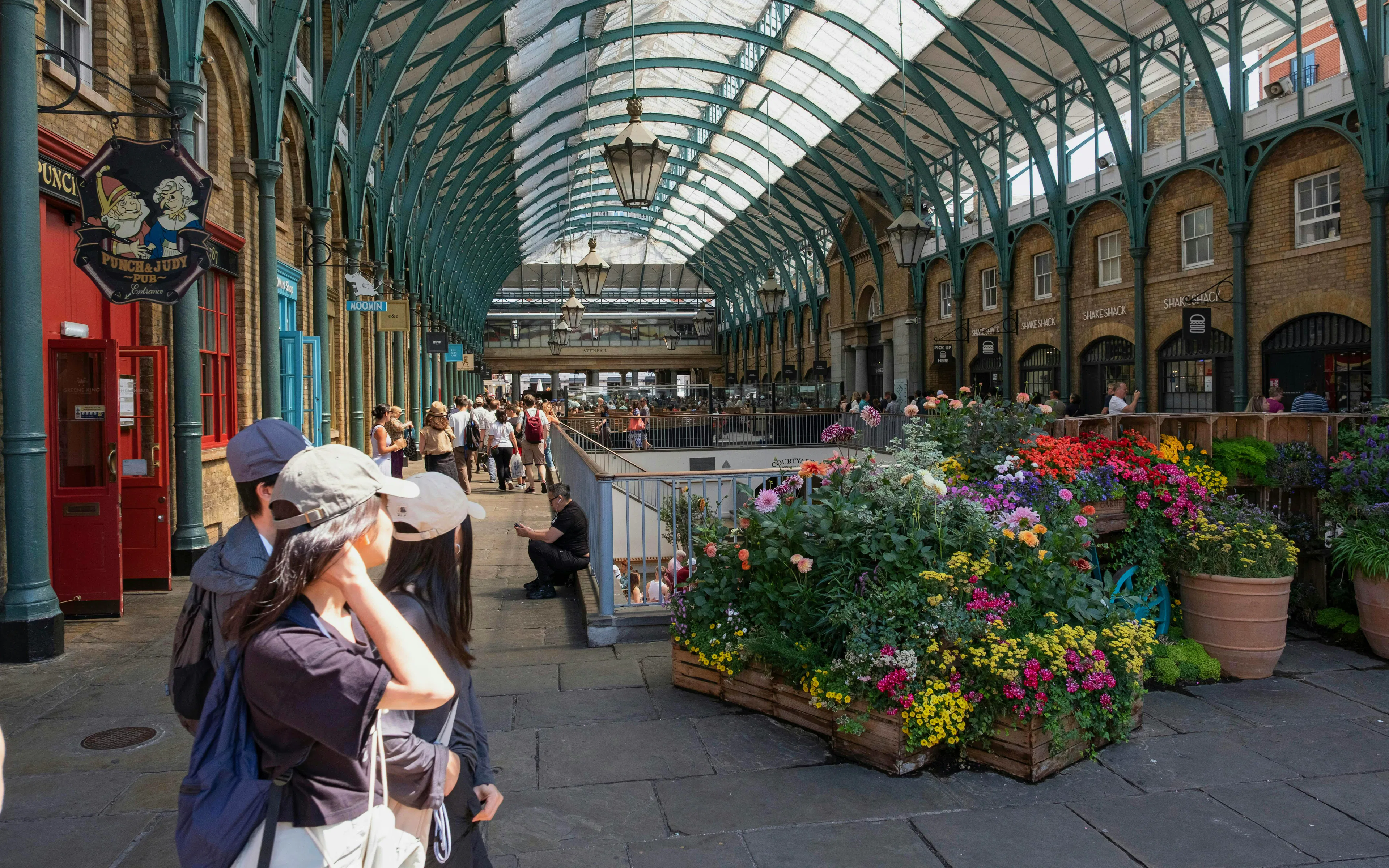 Covent Garden Market in London with tourists and colorful flower displays.