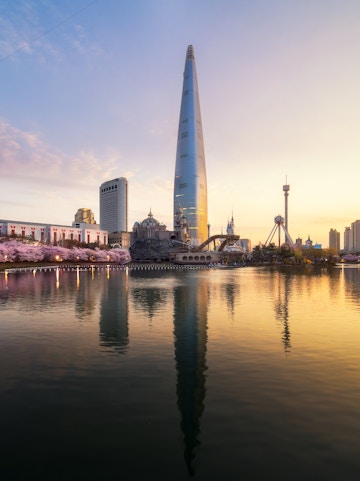 Sunrise over cherry blossoms and tower reflecting in a park lake.