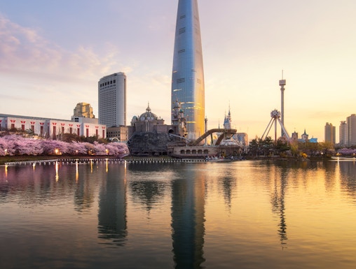 Sunrise over cherry blossoms and tower reflecting in a park lake.