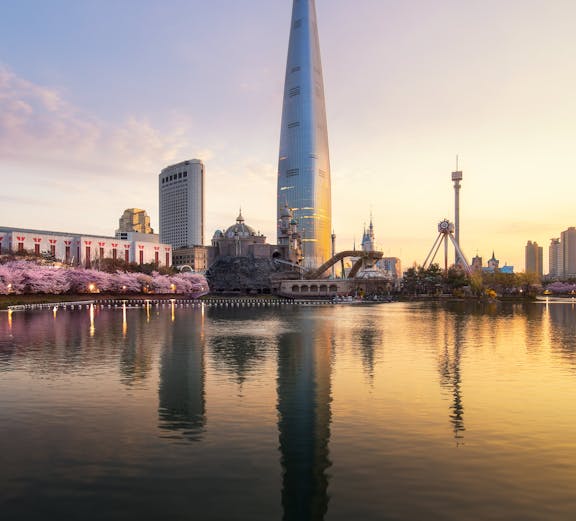 Sunrise over cherry blossoms and tower reflecting in a park lake.