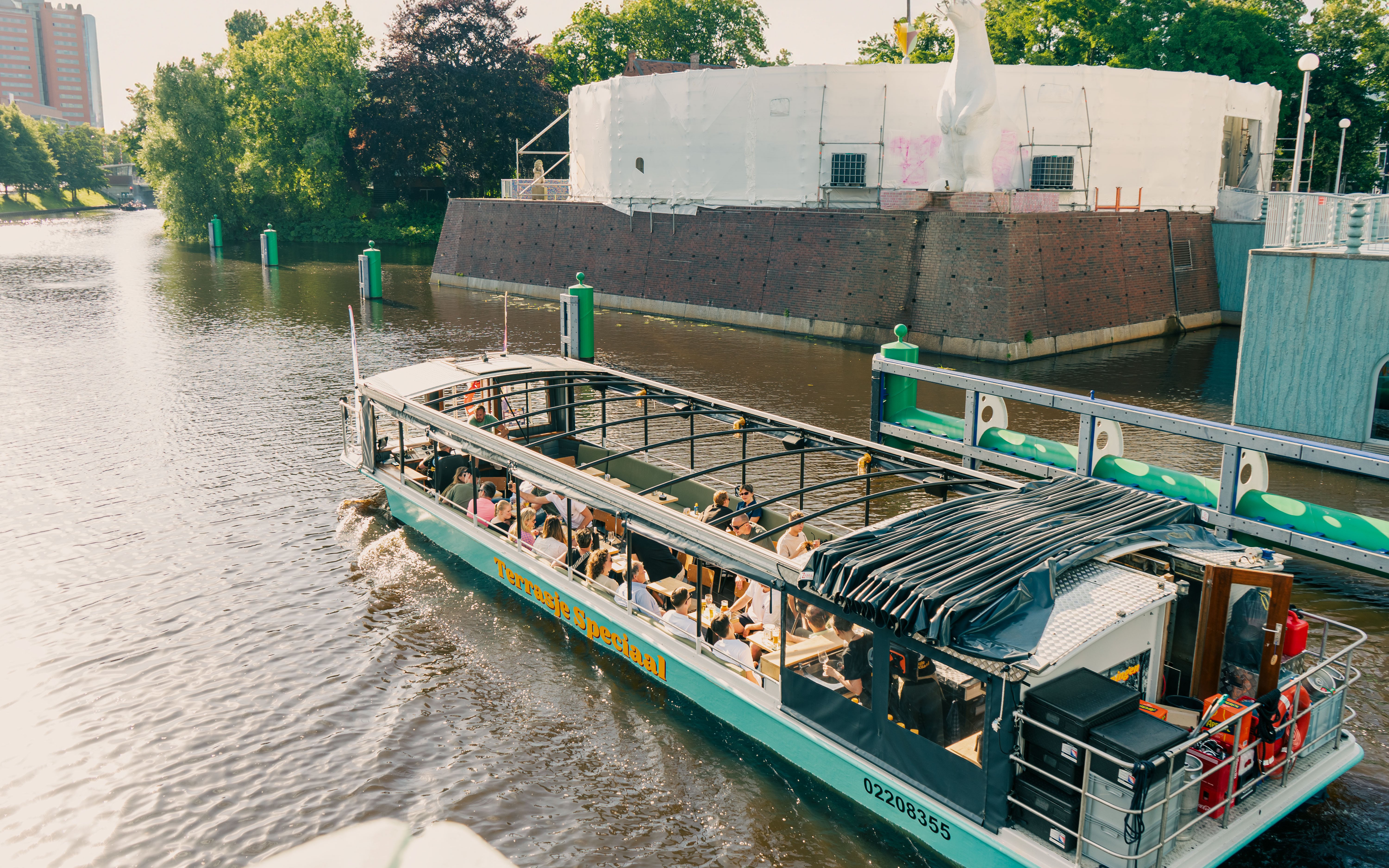 Groningen canal boat with passengers enjoying drinks near a historic building.