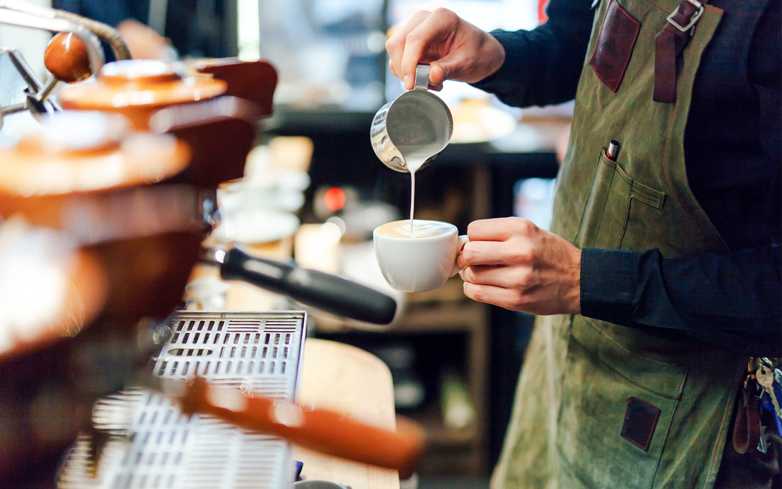 Barista pouring milk into coffee cup at a coffee shop.