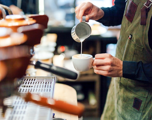 Barista pouring milk into coffee cup at a coffee shop.